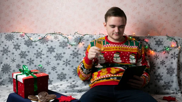 Yeni yıl tatili, genç bir adam bir hediye açar ve paketler, şampanya, yeni yıl hediyeleri, yeni yıl süslemeleri ve aile ile bir sohbet, online tablet