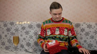 Yeni yıl tatili genç adam bir hediye açar ve paketler, şampanya, yeni yıl hediyeleri, yeni yıl süsleri ve iyi bir ruh hali ve siyah bir kedi.