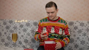 Yeni yıl tatili, genç bir adam bir hediye açar ve paketler, şampanya, yeni yıl hediyeleri, yeni yıl süslemeleri ve iyi bir ruh hali.