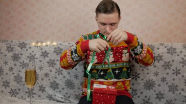 Yeni yıl tatili, genç bir adam bir hediye açar ve paketler, şampanya, yeni yıl hediyeleri, yeni yıl süslemeleri ve iyi bir ruh hali.