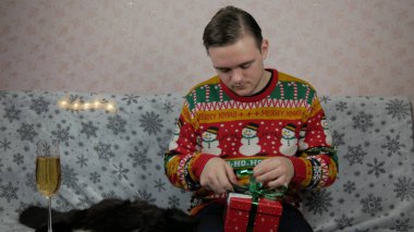 Yeni yıl tatili genç adam bir hediye açar ve paketler, şampanya, yeni yıl hediyeleri, yeni yıl süsleri ve iyi bir ruh hali ve siyah bir kedi.