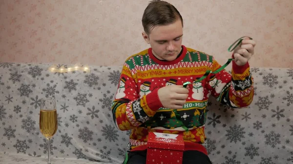 Yeni yıl tatili, genç bir adam bir hediye açar ve paketler, şampanya, yeni yıl hediyeleri, yeni yıl süslemeleri ve iyi bir ruh hali.