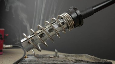 Elektronik lehimleme istasyonu, lehimleme demiri bir tripodun üzerinde duruyor ve ısındığı için duman çıkıyor.