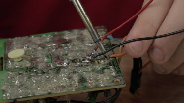 Genç bir usta mikro devreyi tamir eder, lehim makinesini elinde tutar ve tamir eder.