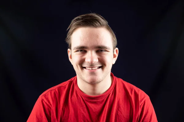 Sıradan tişörtlü genç yakışıklı, soyutlanmış karanlık arka planda duruyor, kızgın ve düşünceli, somurtkan yüzlü.