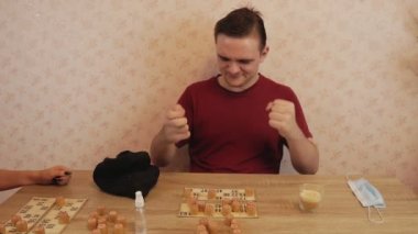 Sovyet loto oyunu, doğrulanmamış fıçılar ve numaralar, kırmızı tişörtlü bir adam loto oynar, kahve, tıbbi maske ve el dezenfektanı olan masada.