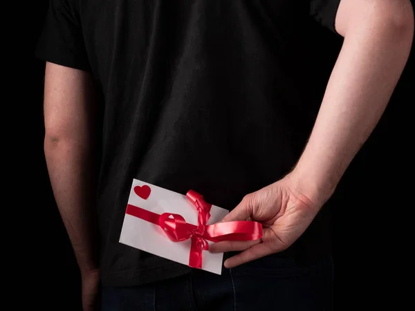 a young guy in a black t-shirt suit holds a white card behind his back on a black background
