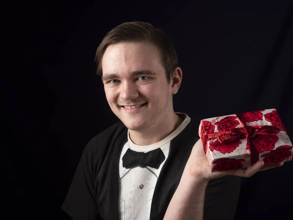 a young guy in a black t-shirt suit holds a red gift in his hand on a black background