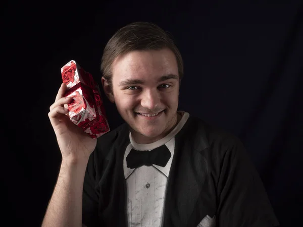 young guy in black t-shirt suit shakes a red gift with surprise on a black background