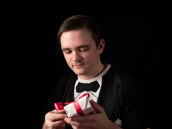 young guy in a black t-shirt suit opens a white gift on a black background