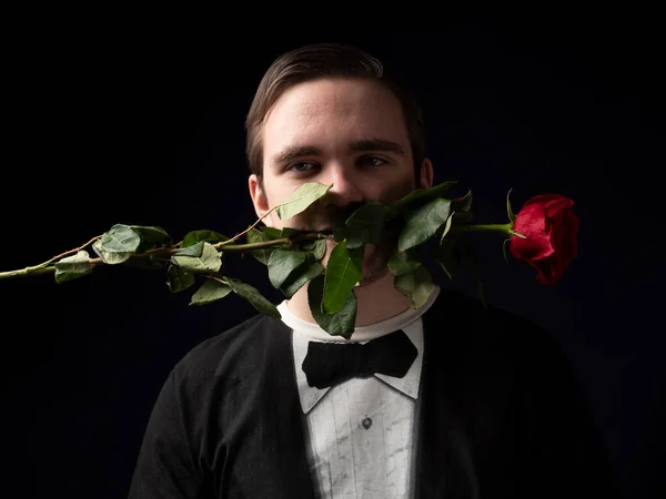 Young guy in a black t-shirt suit holding a red rose in his teeth on a black background