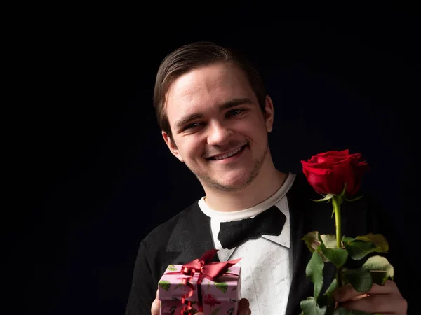 Молодий Хлопець Чорному Костюмі Червоною Трояндою Рожевим Подарунком Руках Посміхається — стокове фото