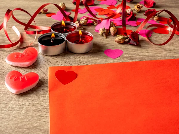 Masada kırmızı gül yaprakları ve kalplerle mumların yanında kırmızı bir zarf.