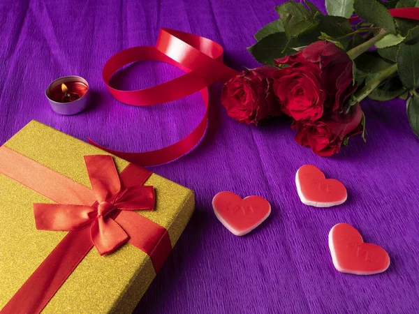 紫の背景にハートとリボンと赤いバラの横にある黄色の贈り物 — ストック写真