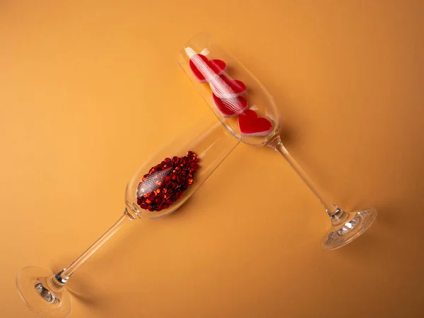 İki bardak yan yana yatar ve biri kırmızı, diğeri turuncu arka planda kırmızı kalplidir.