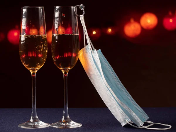 İki kadeh şampanya, bir bardak yüzük ağırlığında ve siyah bir zemin üzerinde mavi bir tıbbi maske.