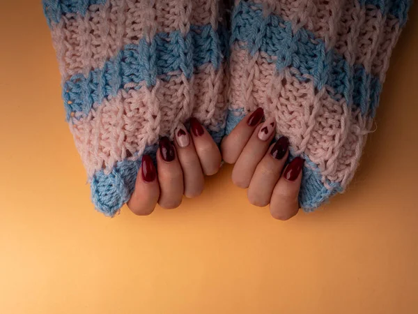 Şık bir kadın manikürü. Genç kadın elleri yünlü kumaşları tutuyor. Kırmızı manikürlü tırnaklar ve turuncu arka planda beyaz kalpler. Bir salgın sırasında evde manikür