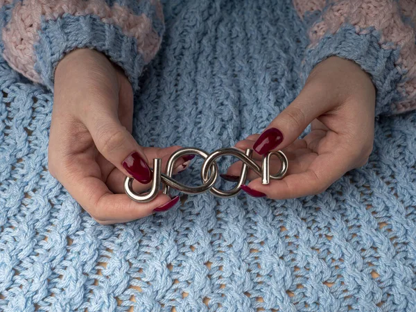 Şık bir kadın manikürü. Yünlü kumaş içindeki genç kadın elleri metal bir yapboz tutuyor. Kırmızı manikürlü tırnaklar ve mavi yün arka planda beyaz kalpler. Bir salgın sırasında evde manikür