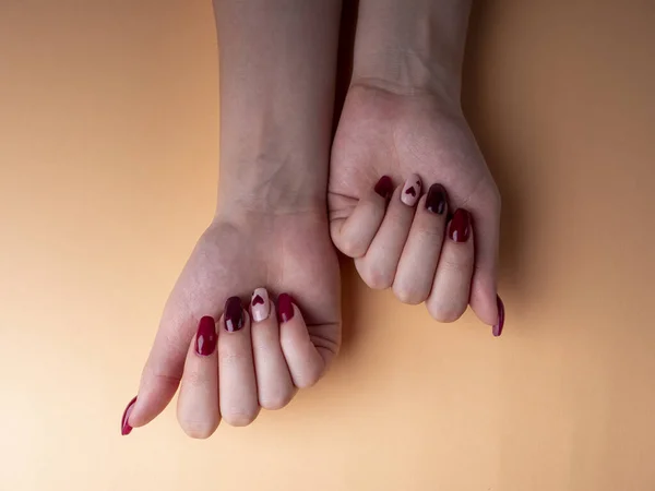 时髦的女性修指甲 年轻的女性手 红白相间 有红白相间的指甲 有心脏 背景橙色 大流行病期间在家里修指甲 — 图库照片