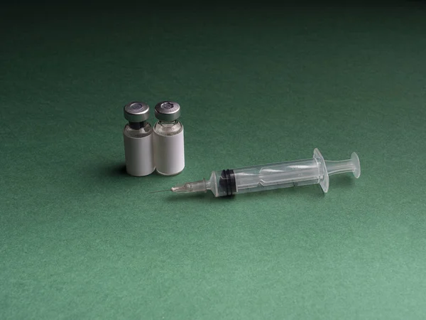 两个玻璃瓶 旁边放着一个装有疫苗的液体和一个注射器 绿色和黑色背景的玻璃瓶和注射器 — 图库照片