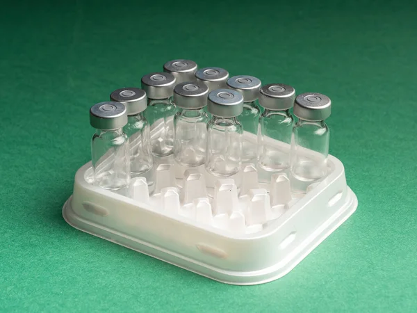 Aşı sıvısının otomatik sıvı dağıtıcının tepsisinde olduğu cam şişeler. Cam şişeler yeşil arka planda.
