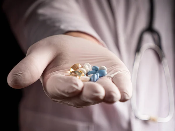 Various pills lie in the outstretched hand of the young doctor. selective focus on outstretched arm with pills