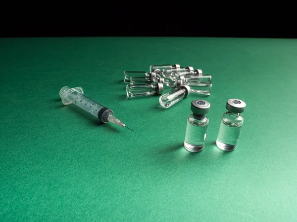 玻璃瓶旁边有一个装有疫苗的液体和一个注射器 放在绿色和黑色的背景上 — 图库照片
