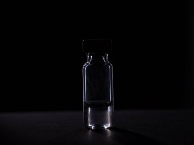 İçinde aşı olan bir sıvı bulunan cam bir şişe. Siyah arkaplanda izole