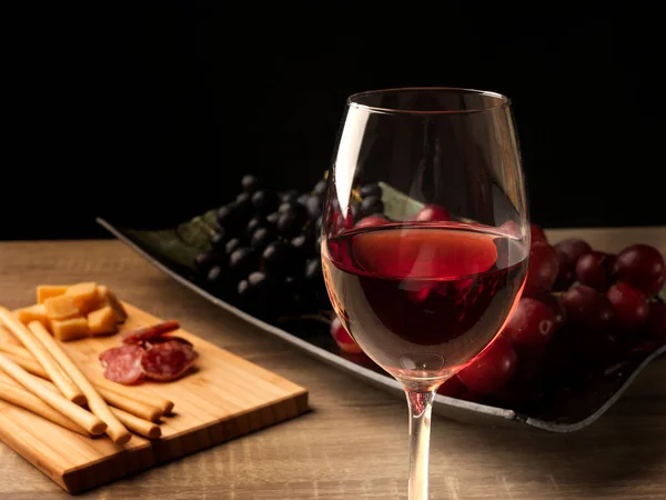 Gül şarabıyla dilimlenmiş salam ve peynir, iki çeşit üzüm, ve tepside İtalyan Grissini, ve ahşap bir masada, siyah arka planda. Üst görünüm düzlüğü