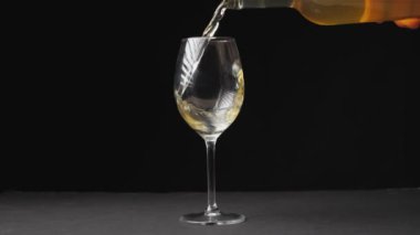 Beyaz şarap, siyah arka plandaki bir şarap bardağına dökülüyor. Şarabı bardağa doldurmanın yavaş hareketi.
