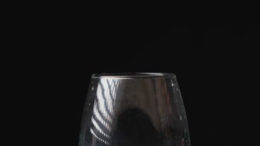Beyaz şarap, siyah arka plandaki bir şarap bardağına dökülüyor. Şarabı bardağa doldurmanın yavaş hareketi. Yakın çekim..