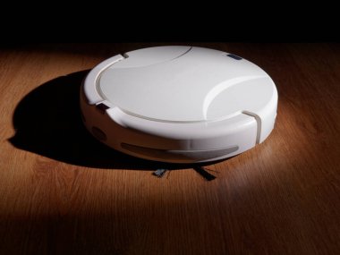 Robot elektrikli süpürge ahşap parke zeminde duruyor, ev temizliği kavramı.