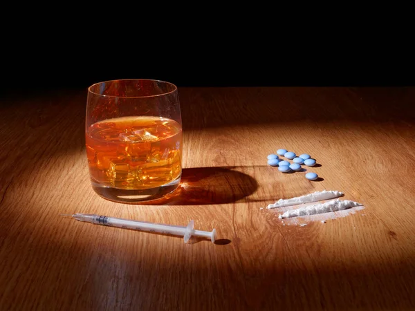 Bardakta buzlu viski, haplar ve uyuşturucular yakınlarda, alkol ve uyuşturucunun insan vücuduna verdiği zarar kavramı