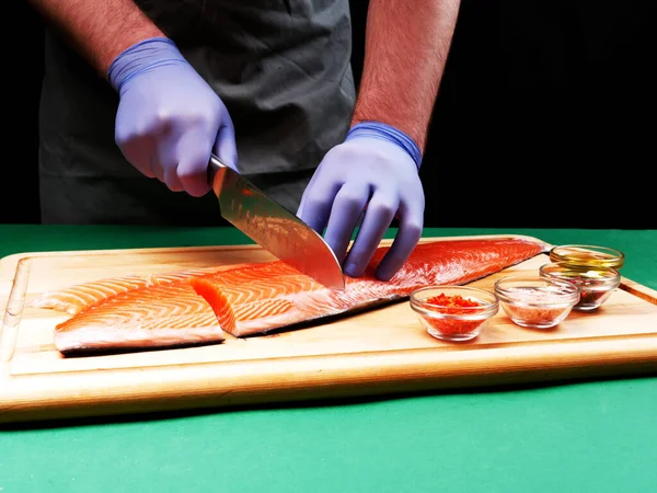 A young chef cuts a fresh raw salmon fillet and spices lie nearby on a wooden cutting board. Healthy food concept