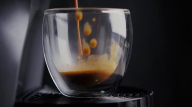 Kahve makinesinde bir fincan var ve içine koyu kahve dökülüyor. Siyah arkaplanda izole