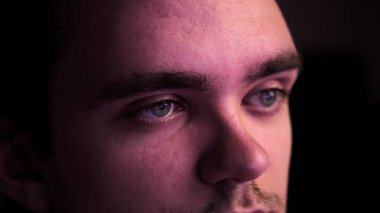 Karanlıkta oturup televizyon izleyen genç bir adamın yakın çekimi. Rahatlama ve hafta sonu konsepti