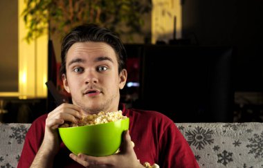 Kırmızı tişörtlü genç bir adam beyaz bir battaniyenin olduğu kanepede oturur ve patlamış mısır yer ve televizyon izlemekten korkar. Hafta sonu ve rahatlama kavramı