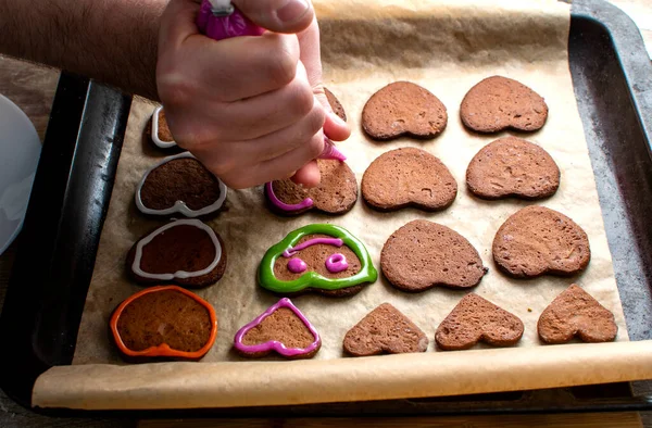 Genç bir şef zencefilli kurabiyeleri pembe kremayla süslüyor, gözleri ve ağzı çiziyor.