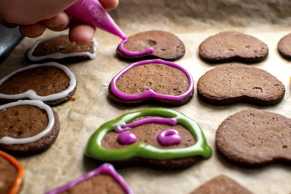 Genç bir şef zencefilli kurabiyeleri pembe kremayla süslüyor, gözleri ve ağzı çiziyor.