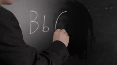 Siyah takım elbiseli bir öğretmen tahtaya alfabenin İngilizce harflerini yazar. Okul kavramı