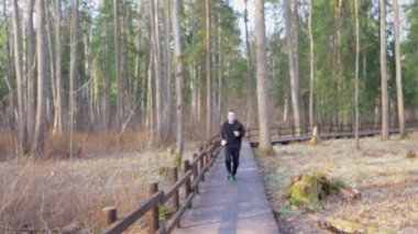 Siyah eşofmanlı bir adam kahverengi ahşap bir köprüden geçiyor. Sağlıklı yaşam tarzı kavramı