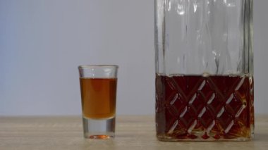 Tahta bir masanın üzerinde bir sürahi ve iki bardak var, erkek iki bardak alıyor ve içlerindeki sıvıyı döküyor, sonra da geri koyuyor. Alkol ve rahatlama kavramı