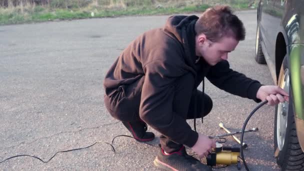 Cara Jovem Infla Uma Roda Carro Com Uma Bomba Elétrica — Vídeo de Stock