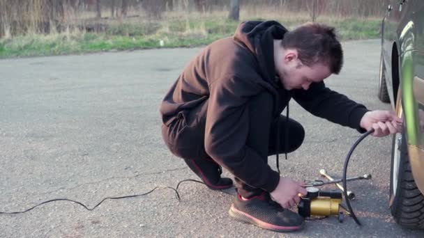 Cara Jovem Infla Uma Roda Carro Com Uma Bomba Elétrica — Vídeo de Stock