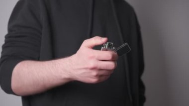 Siyah eşofmanlı bir adam benzinli metal bir çakmak yakıyor ve sonra da yangını söndürüyor.