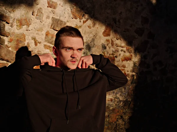 Sokakta siyah eşofmanlı genç adam, güneşe bakıp gülümsüyor, eski bir değirmenin içinde, spor hayatı konseptinde..