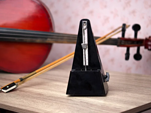 Siyah, klasik bir metronom masanın üzerinde dururken ritmi çalar, arkada bir çello yatar, yakın plan bir müzik aleti konsepti..