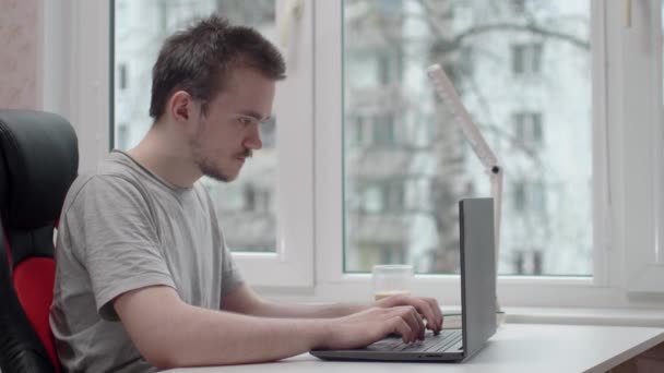 Jovem Está Digitando Computador Ele Está Vestindo Uma Camiseta Cinza — Vídeo de Stock