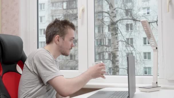 Joven Está Bebiendo Café Mirando Por Ventana Lleva Una Camiseta — Vídeos de Stock