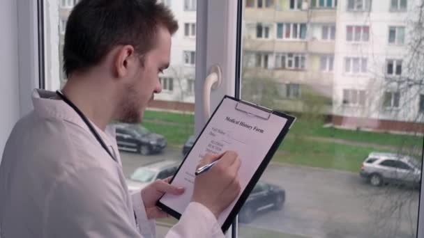 Junger Arzt Füllt Patientendaten Fenster Vor Dem Hintergrund Des Gebäude — Stockvideo